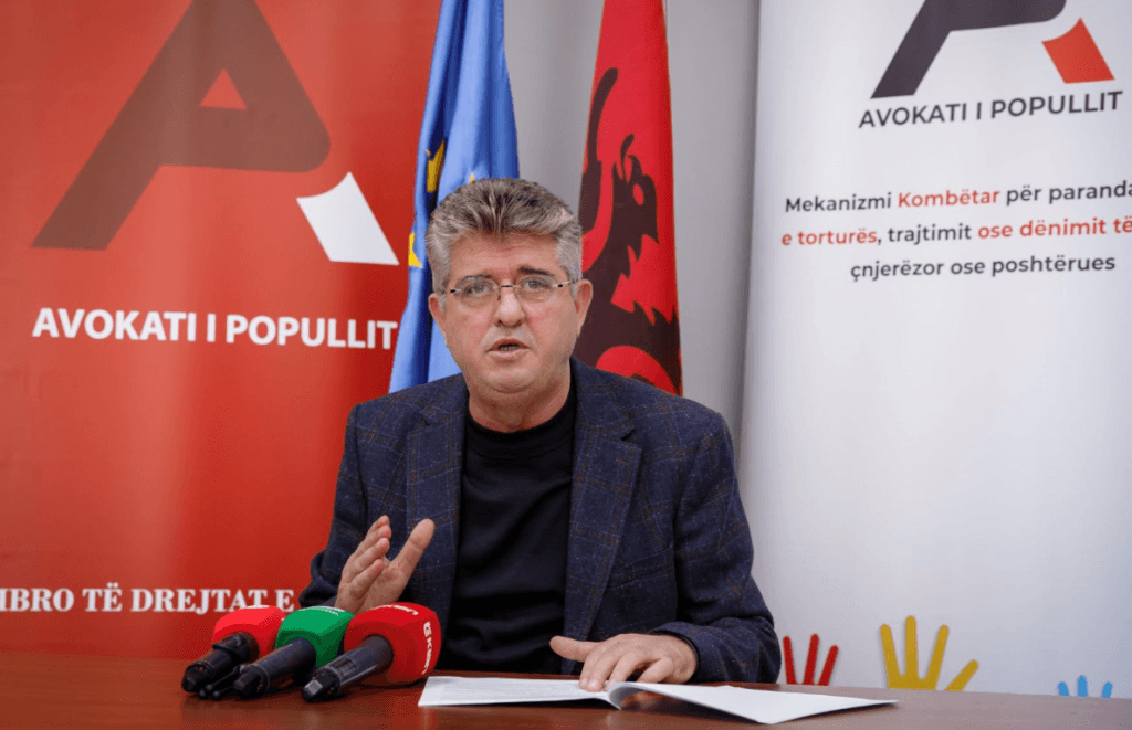 A representative of the Ombudsman speaks at a news conference in front of microphones, with the institution's logo behind him