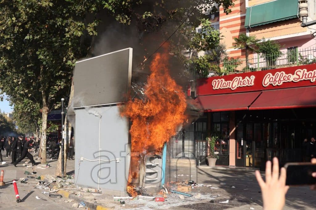 A kiosk burns on the sidewalk next to a cafe during a protest in Tirana