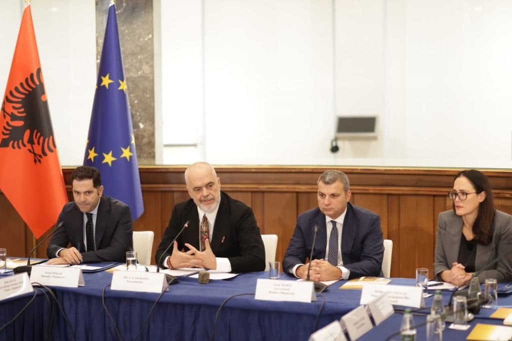 Edi Rama në tryezë mes ministrit Petrit Malaj, guvernatorit Gent Sejko dhe ministres Delina Ibrahimaj, me flamujt shqiptar dhe të BE-së pas tyre